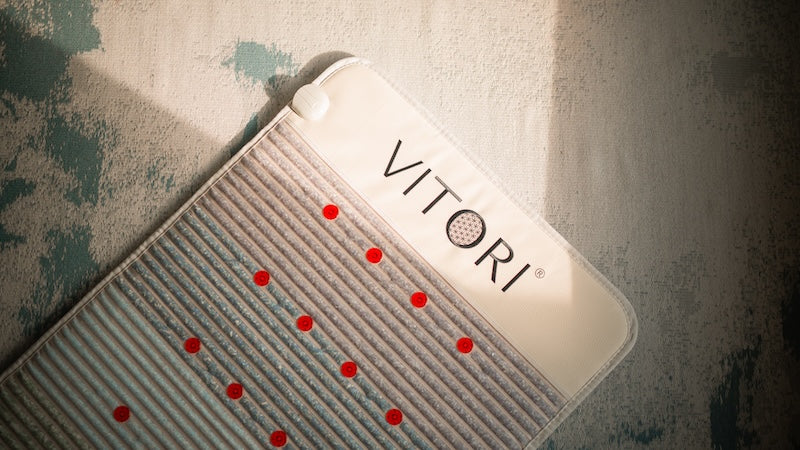 Eine Nahaufnahme einer VITORI® Premium Kristallmatte – Das Original mit horizontalen Rillen und kleinen roten Punkten, platziert auf einer grün-weiß gemusterten Oberfläche, teilweise vom Sonnenlicht beleuchtet.