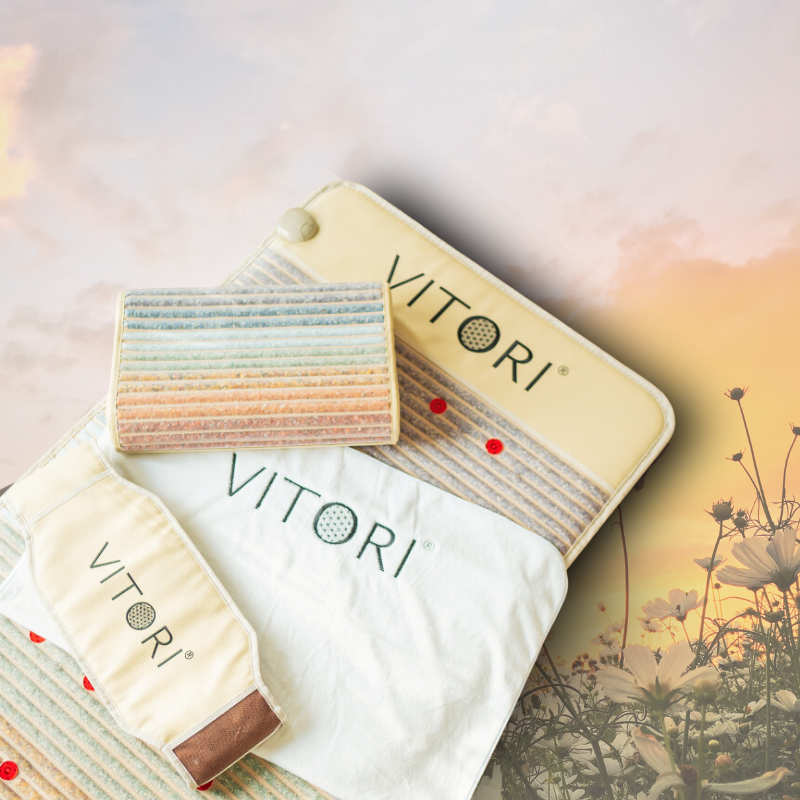 Das VITORI® Paket Deluxe, bestehend aus Beutel, Maske, Kristallkissen und Tuch von VITORI®, wird auf einem pastellgestreiften Hintergrund mit einem Sonnenuntergang und Wildblumen in der Ferne dargestellt.