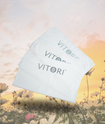 Drei weiße Handtücher mit dem VITORI®-Logo liegen vor einem sanften Sonnenuntergangshimmel. Jedes ist mit dem Bezug für Premium Kristallmatte versehen, die für höchsten Komfort und Hygiene sorgt.